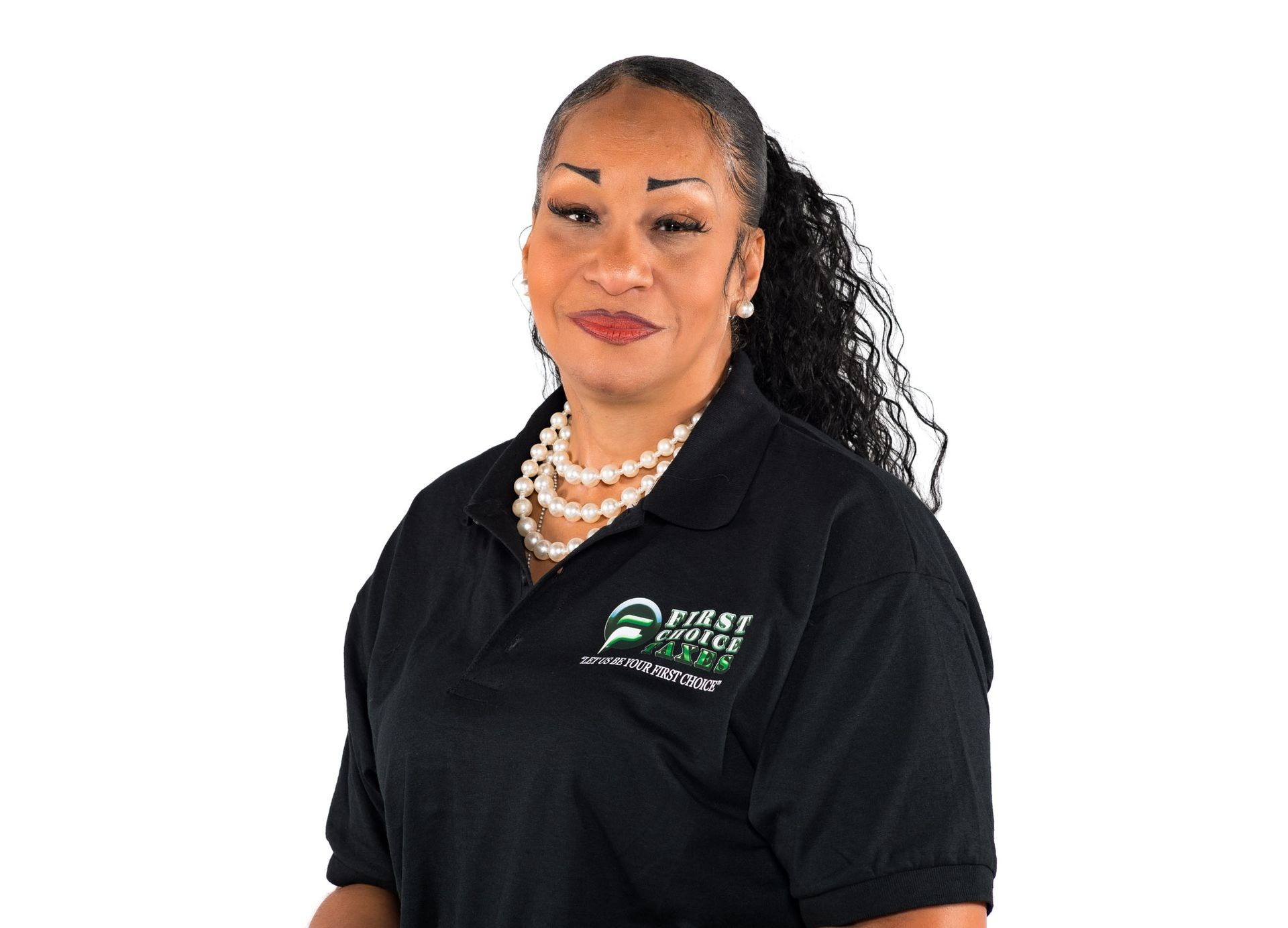 Woman in black polo shirt and pearl necklace smiling against a white background.